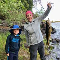 Fishing opener A child and adult standing by a shoreline holding a walleye fish.