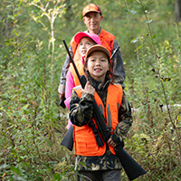 Hunting Safety A family wearing bright orange hunting vests safely carry their firearms in the forest.