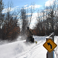 A snowmobiler drives around a corner on an icey snow covered trail.