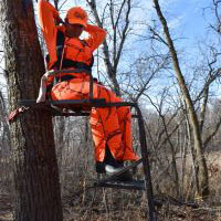 Tree stand safety. A person wearing orange sitting in a tree stand in the woods.